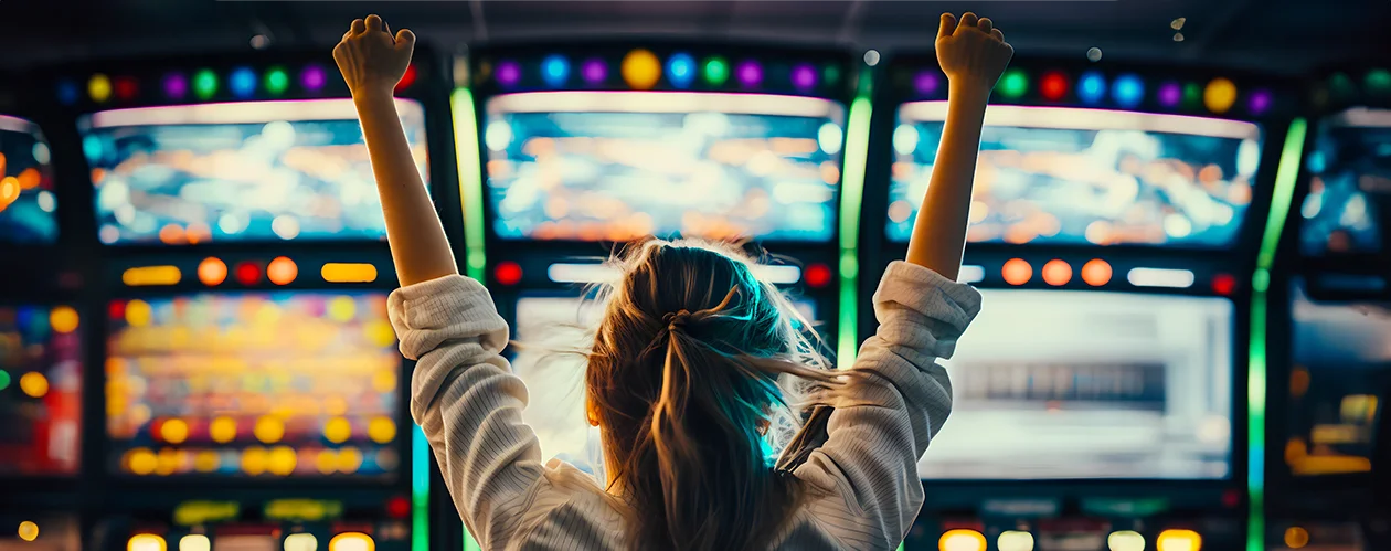 A cinematic, wide-angle shot from behind a young woman, cheering with fists clenched in front of vibrant, brightly lit casino-style slot machines.